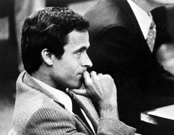 Ted Bundy sentado no tribunal, de paletó, com a mão no queixo
